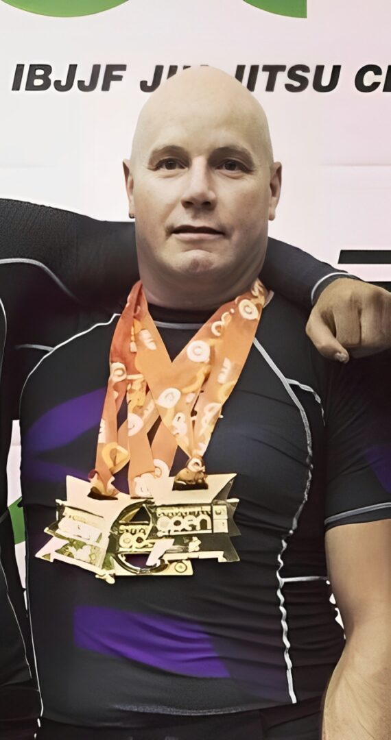 Person wearing a black sports outfit with multiple gold medals around their neck, standing in front of a backdrop with text and graphics.